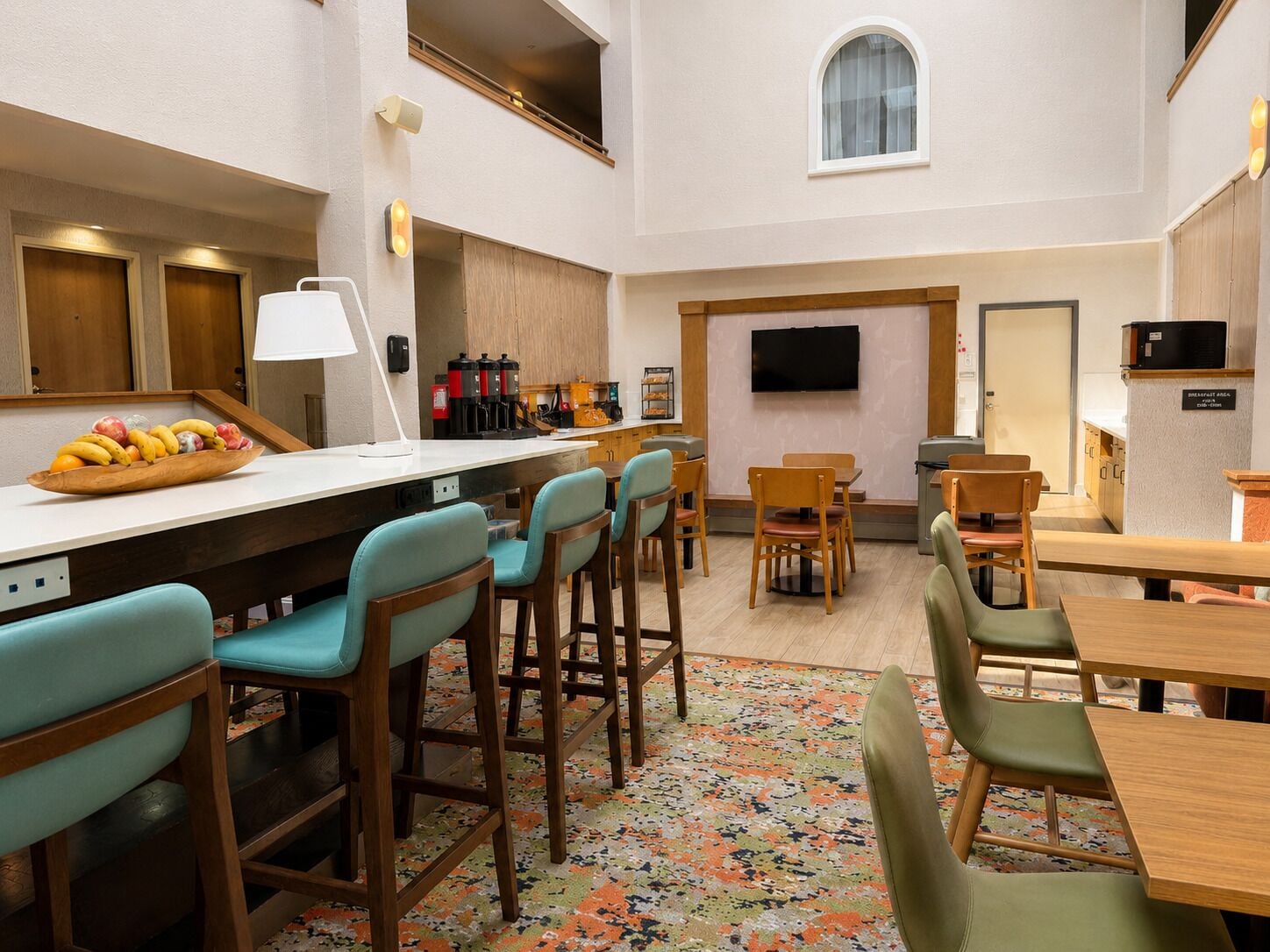 Ein Hotelzimmer mit einer Küchenzeile, einem Flachbildfernseher, einer Obstschale und einem gemusterten Teppich.