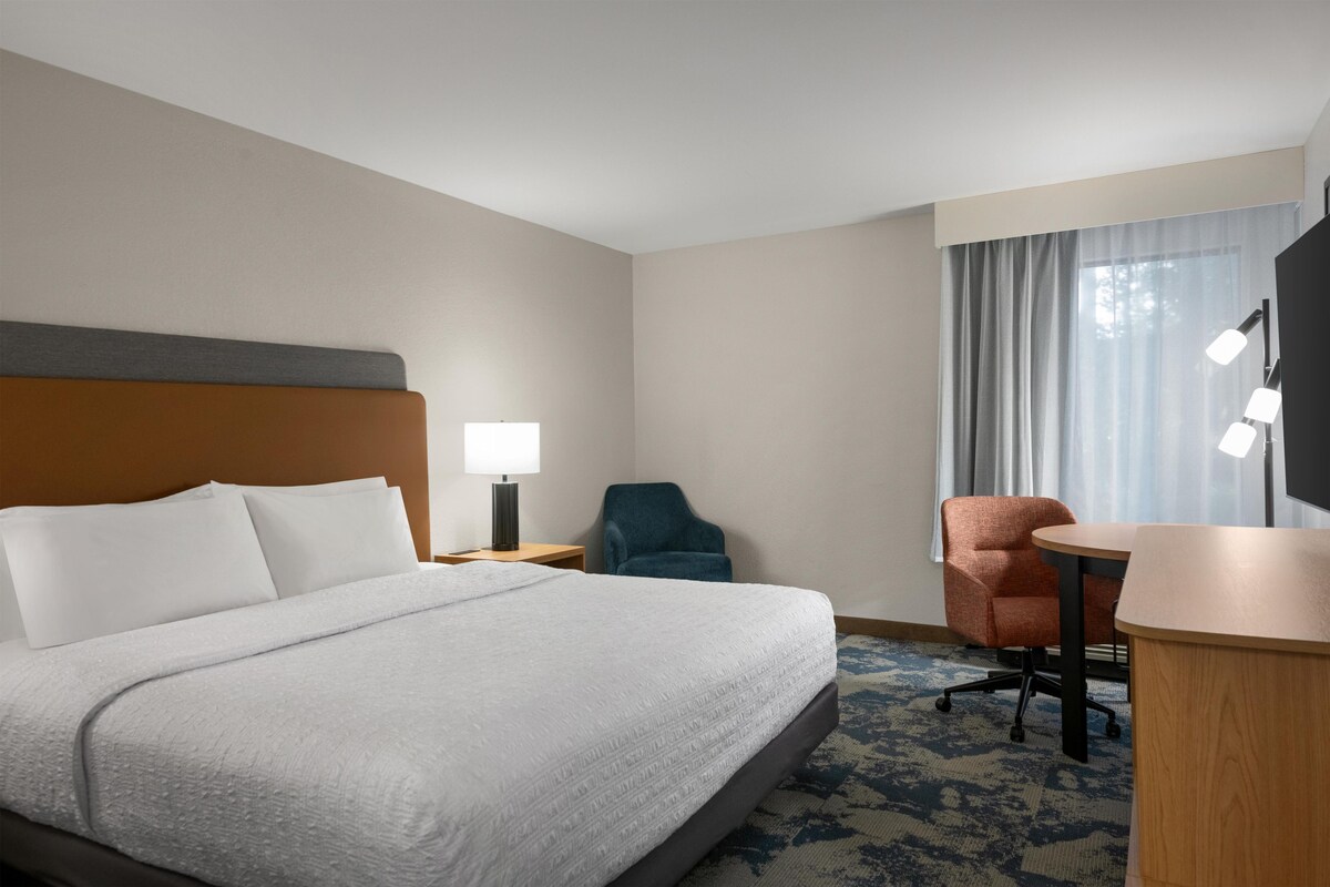 Een hotelkamer met een groot bed, een bureau, twee stoelen, een nachtkastje met een lamp en een televisie.