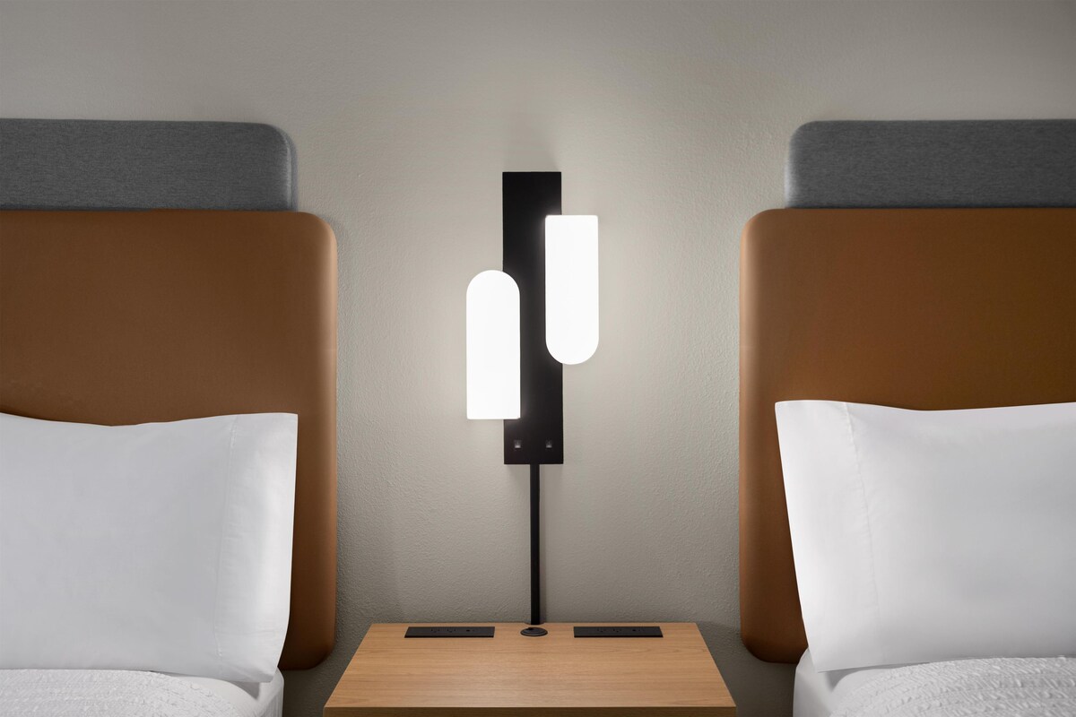 Een hotelkamer met een nachtkastje, een lamp en twee bedden.