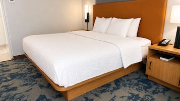 A hotel room with a bed, a bedside table with a lamp, a phone, and a small cabinet.