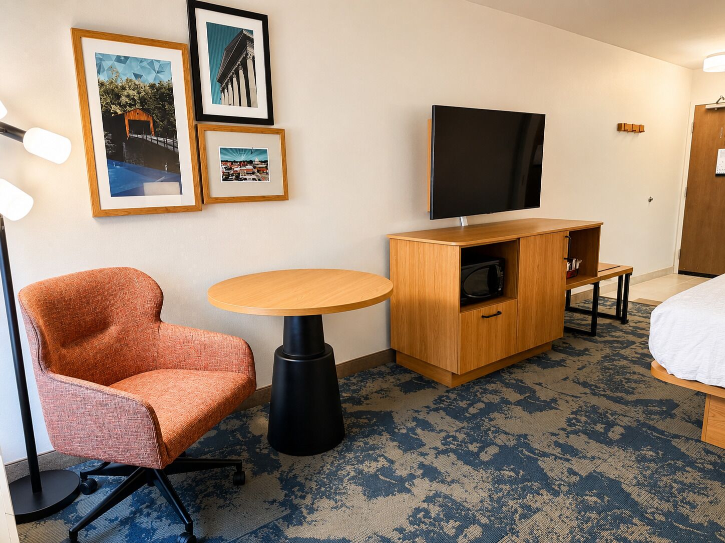 Une chambre d’hôtel avec un lit simple, un petit bureau en bois, une chaise, une télévision et une étagère fixée au mur.