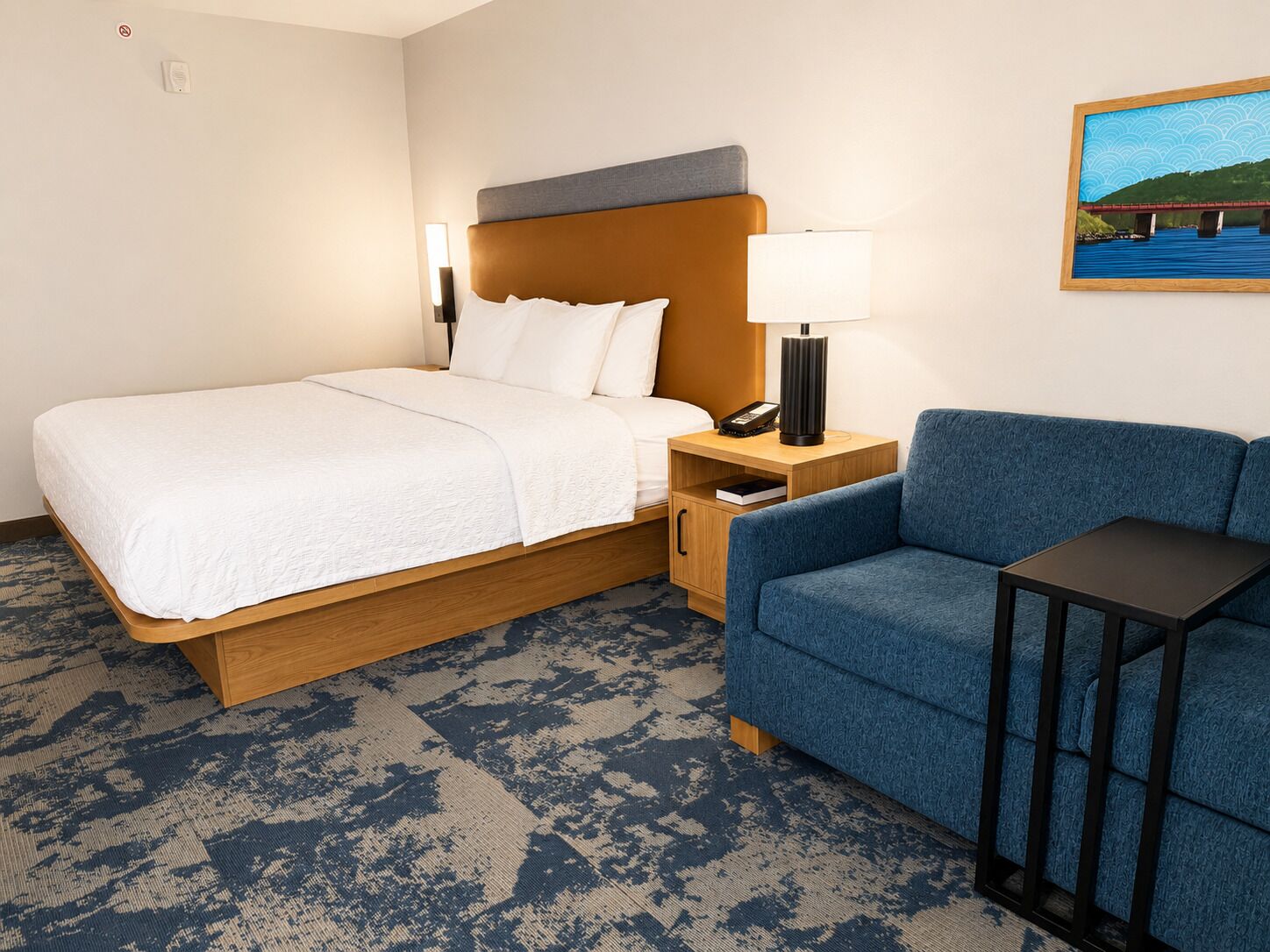 Een hotelkamer met een bed, een blauwe bank, een nachtkastje met een lamp en een schilderij aan de muur.
