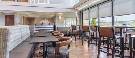 Un restaurante moderno con techo alto, suelo de madera y una zona de estar con mesas y sillas.