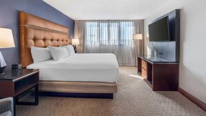 A hotel room with a large bed, a flat-screen TV, a desk with a lamp, and a window with curtains.