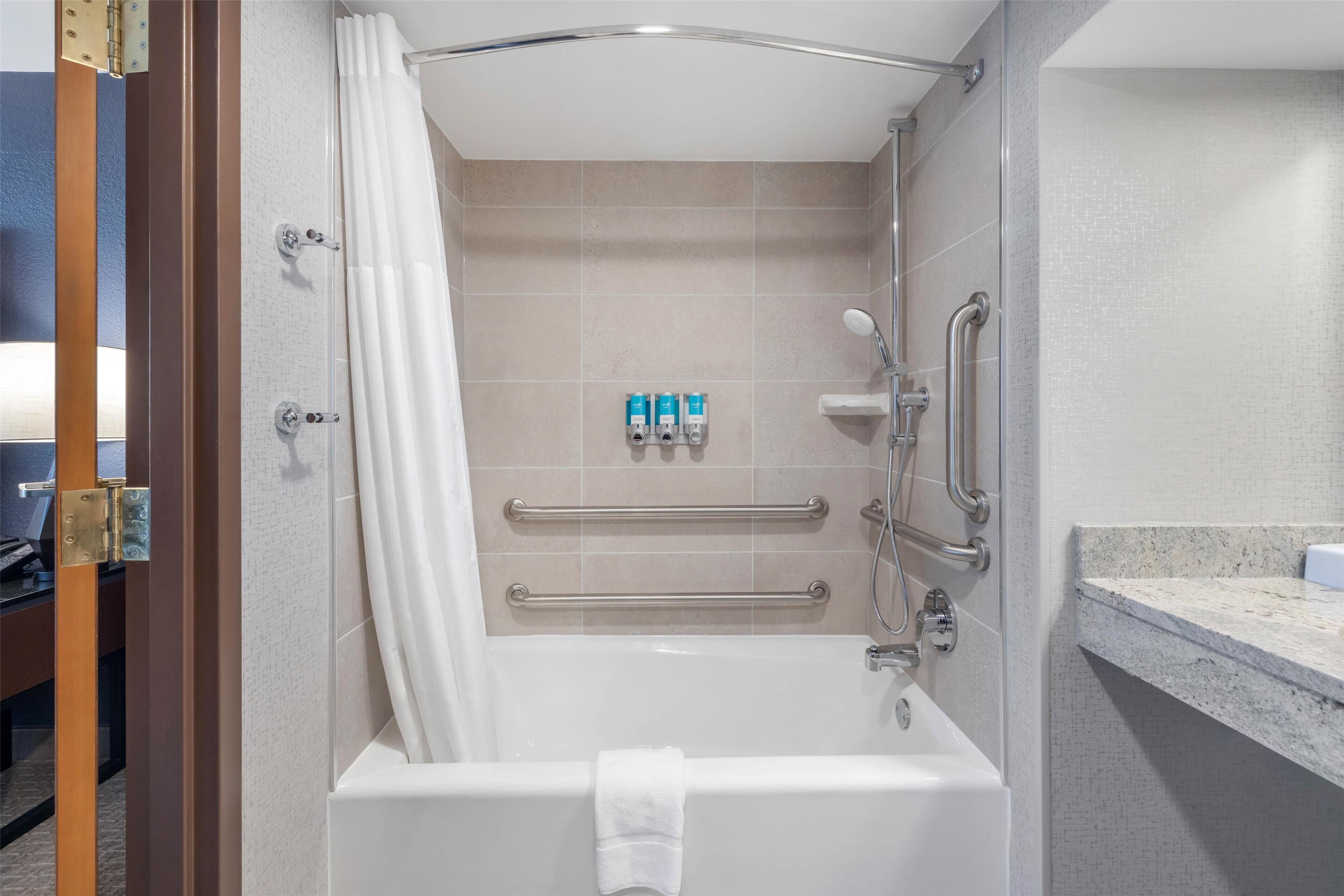 Une salle de bain moderne équipée d’une baignoire, d’une douche et de barres d’appui.