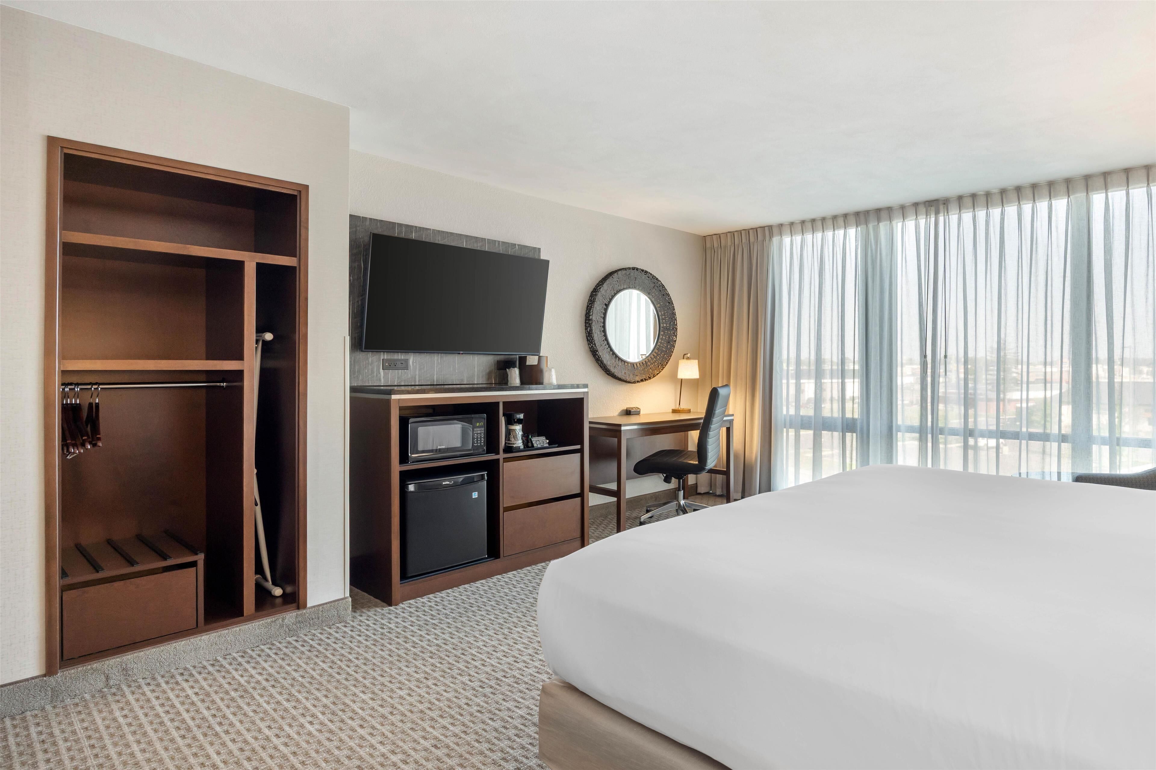 A hotel room with a large bed, a desk with a chair, a TV, a microwave, and a minibar.