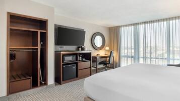 A hotel room with a large bed, a desk with a chair, a TV, a microwave, and a minibar.
