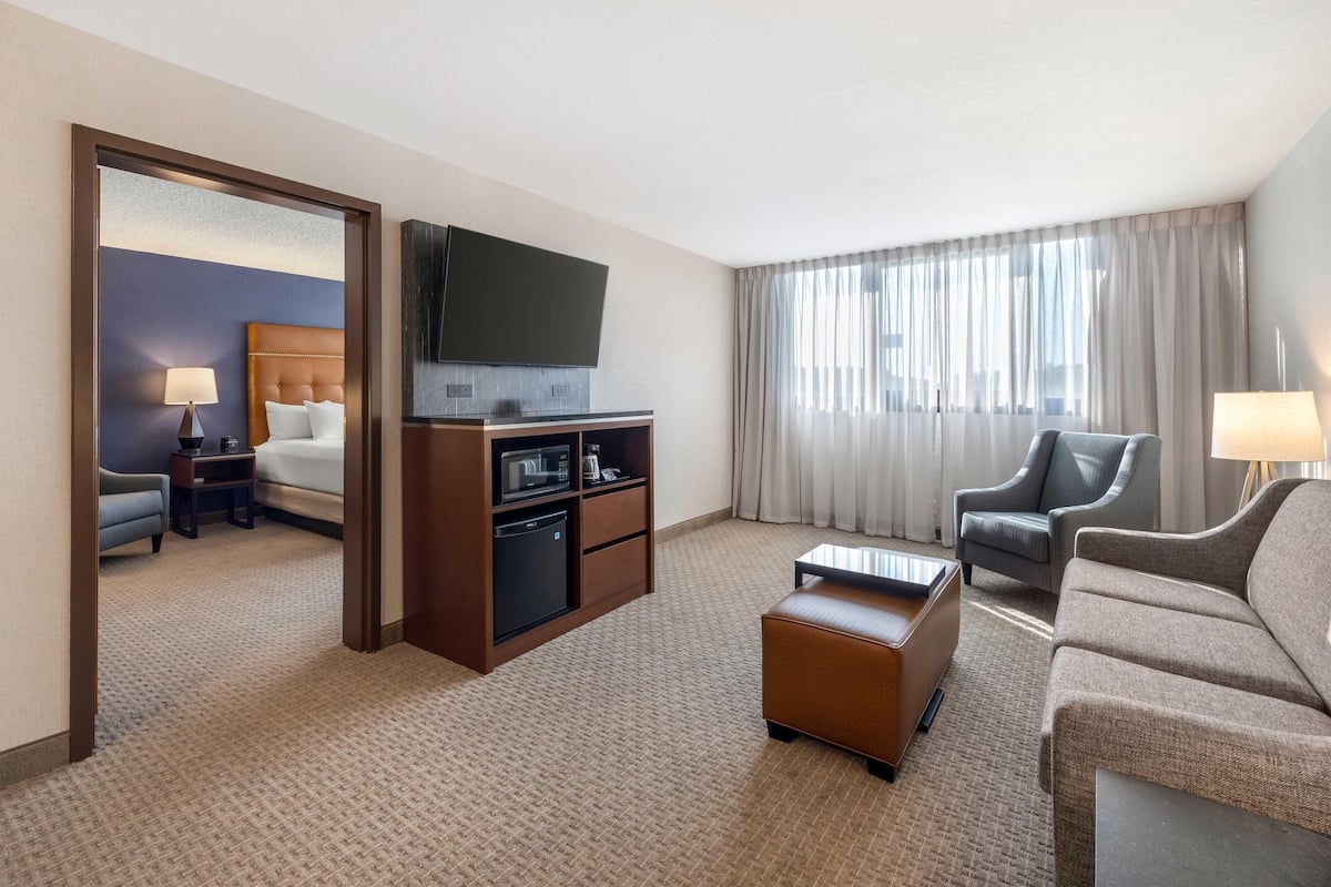 Habitación de hotel con cama, televisión, escritorio, cafetera, sofá y ventana con cortinas.