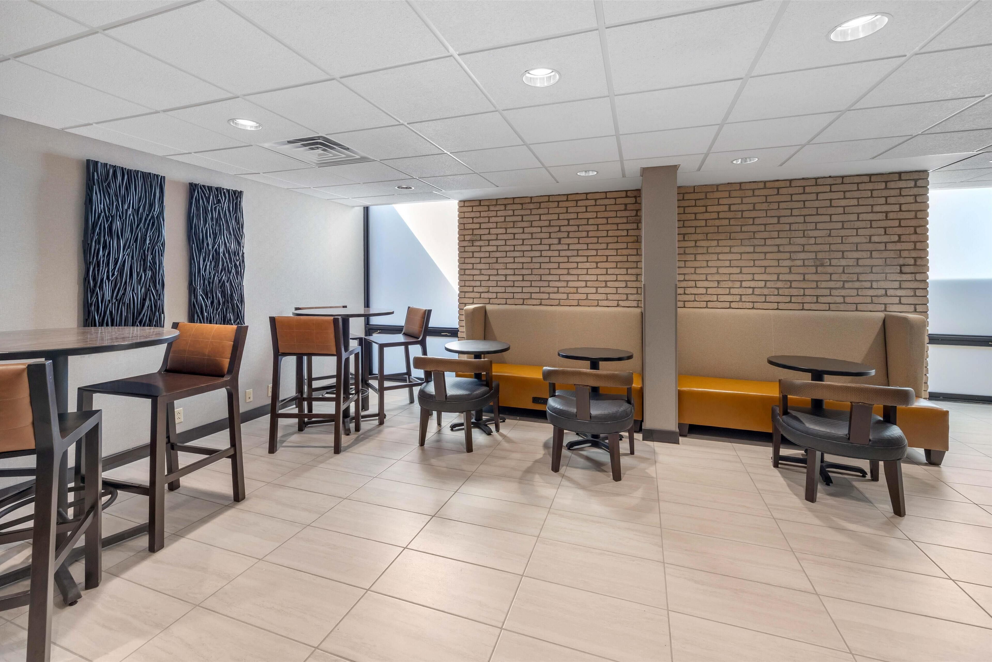 Ein modernes Café-Interieur mit verschiedenen Sitzgelegenheiten, darunter Tische, Stühle und eine gemütliche Sofaecke, sowie einer Ziegelwand als Gestaltungselement.