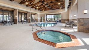 An indoor swimming pool with a hot tub, surrounded by tables and chairs, with a high ceiling and large windows.