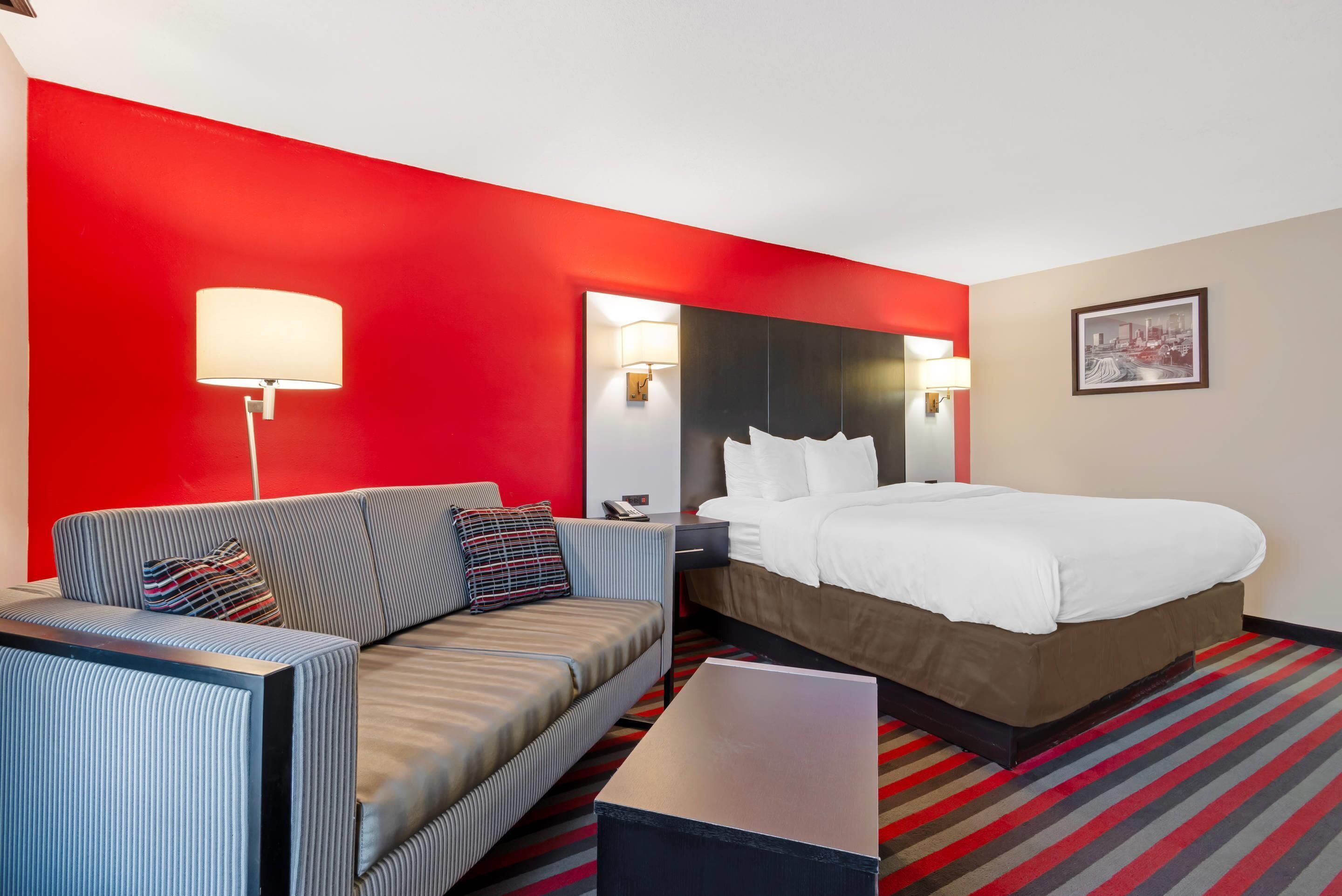 A hotel room with a bed, a sofa, a nightstand, a lamp, and a framed picture on the wall.