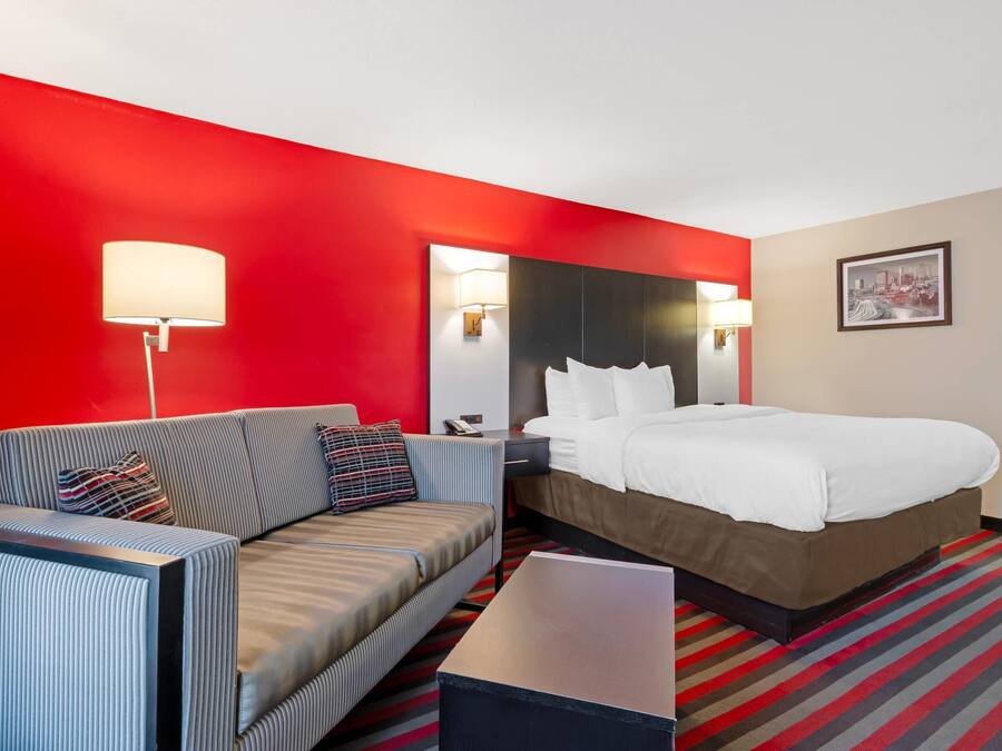 A hotel room with a bed, a sofa, a nightstand, a lamp, and a framed picture on the wall.
