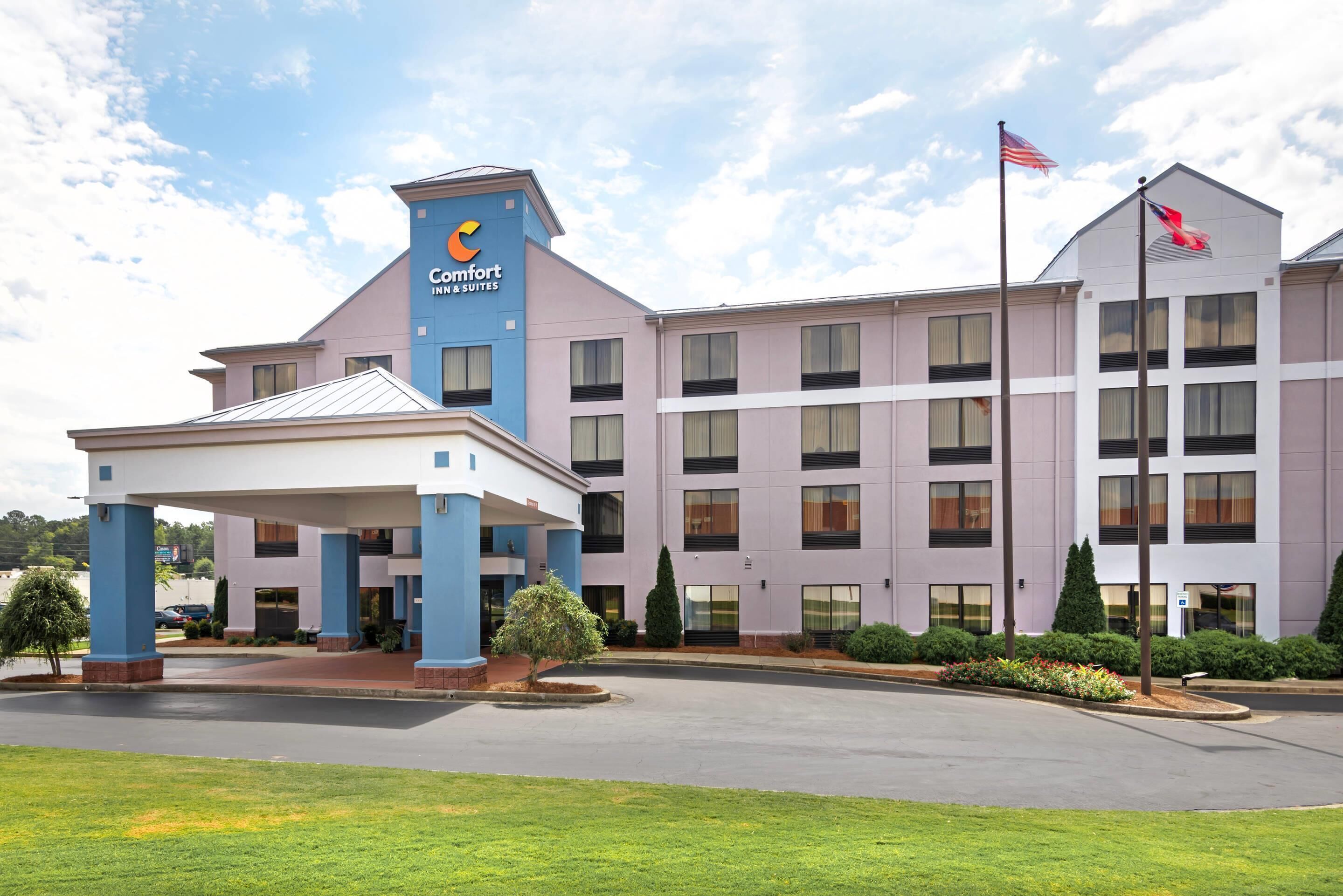 A Comfort Inn & Suites hotel with a modern design, featuring a prominent blue and white color scheme, a covered entrance, and a flagpole with the American flag.