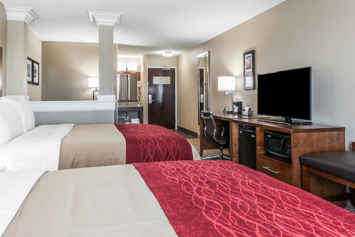 A hotel room with two beds, a desk with a TV, a microwave, and a chair.