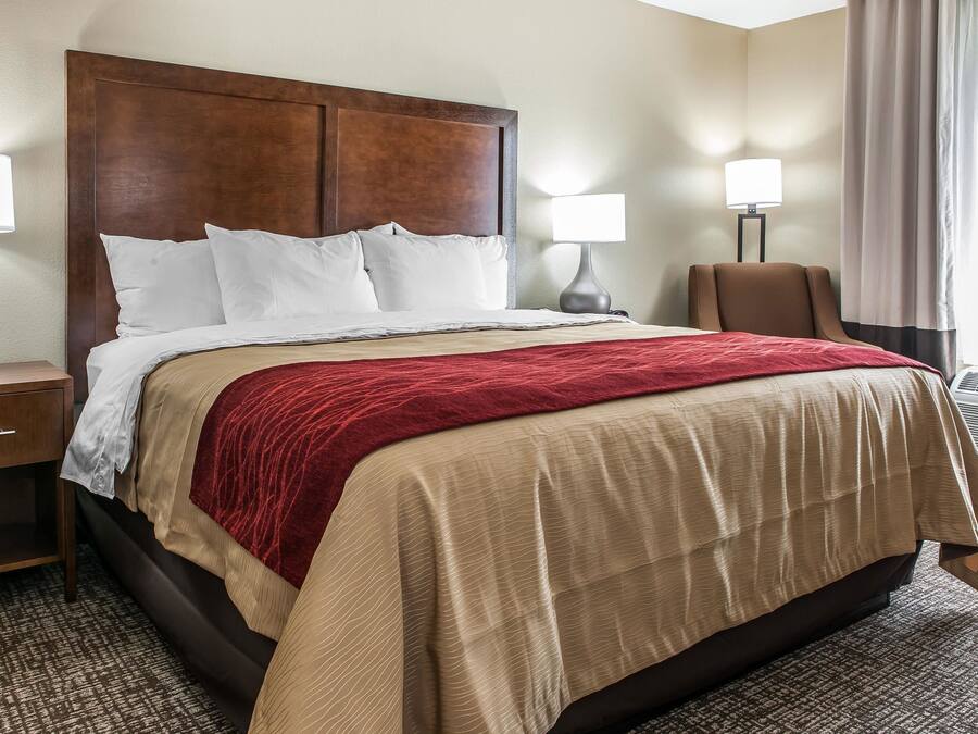 Una habitación de hotel con una cama grande, dos lámparas de noche, una silla y una ventana con cortinas.