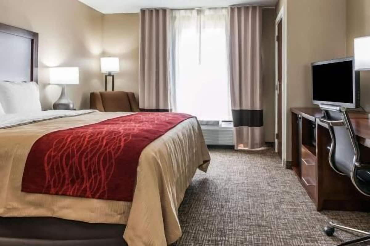 A hotel room with a bed, a desk with a television, a chair, and a window with curtains.