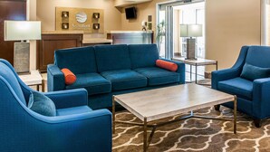 Un hall d’hôtel avec un canapé bleu, des fauteuils, une table basse et un comptoir de réception.