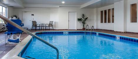 An indoor swimming pool with clear blue water, a lifeguard chair, and a poolside table with chairs.