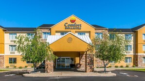 Un bâtiment de la chaîne Comfort Inn & Suites, avec une façade jaune, des éléments en briques et un ciel bleu clair.