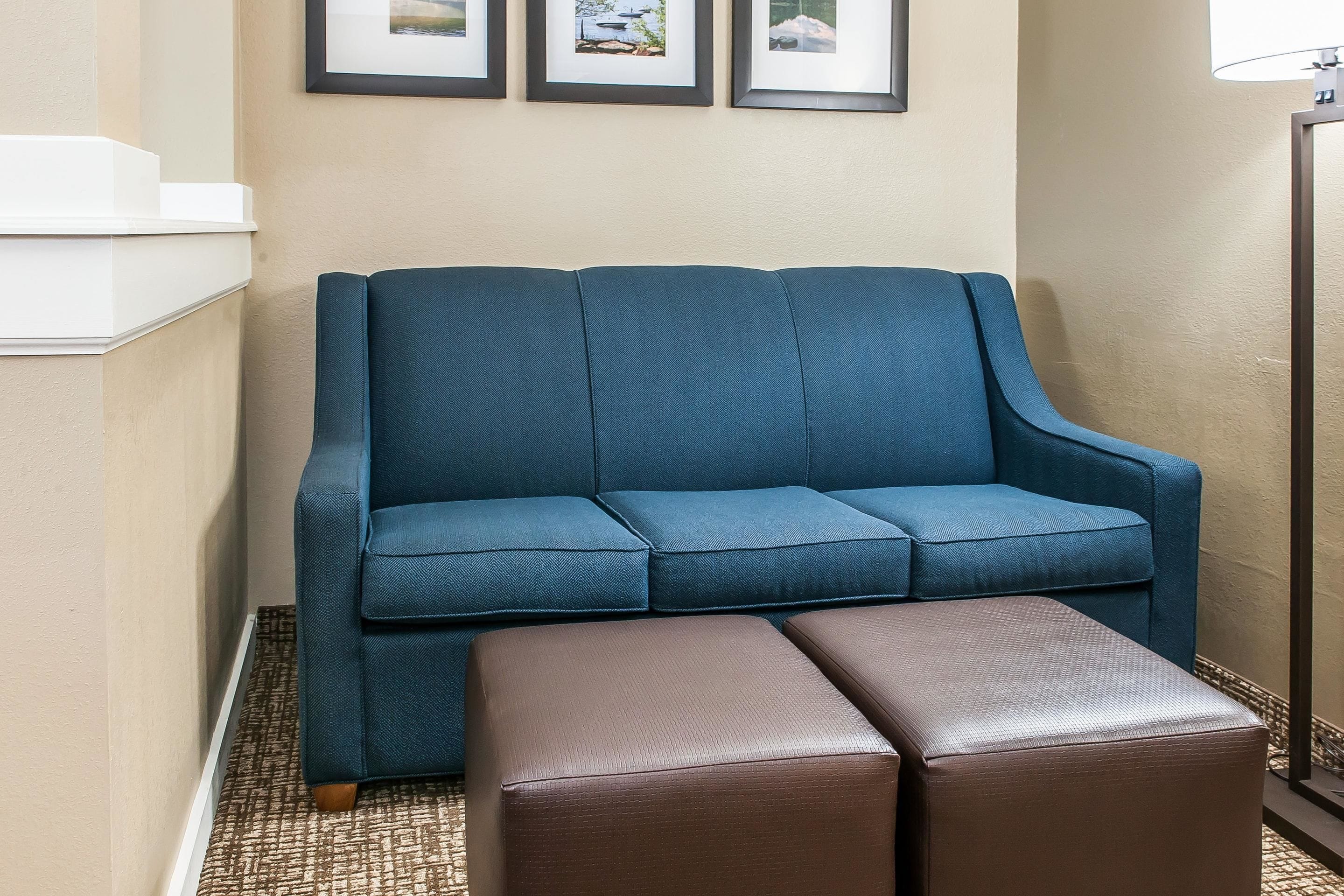 A blue sofa with a matching ottoman in a corner, framed pictures on the wall, and a lamp to the right.