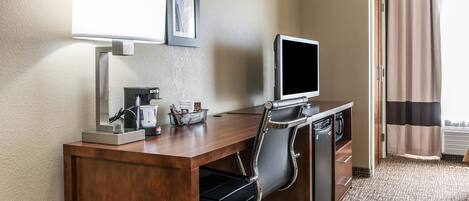 Habitación de hotel con un escritorio de madera, una silla de oficina negra, un televisor de pantalla plana, una cafetera y un cuadro en la pared.