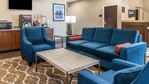 Un hall d’hôtel avec un canapé bleu, un fauteuil et un coin café.