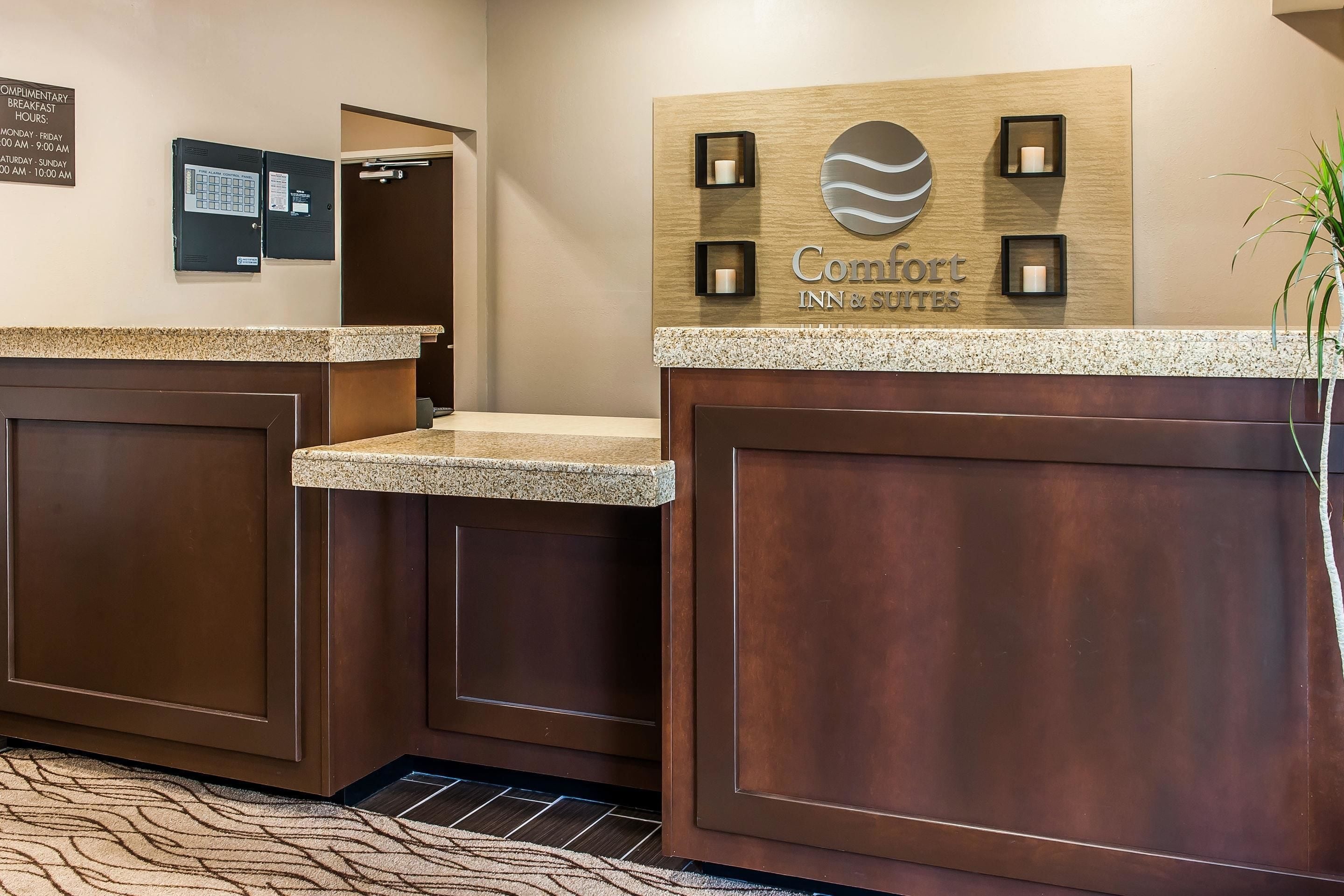 Un hall d’accueil d’hôtel avec un comptoir de réception en bois, un panneau d’affichage et une enseigne indiquant « Comfort Inn & Suites ».