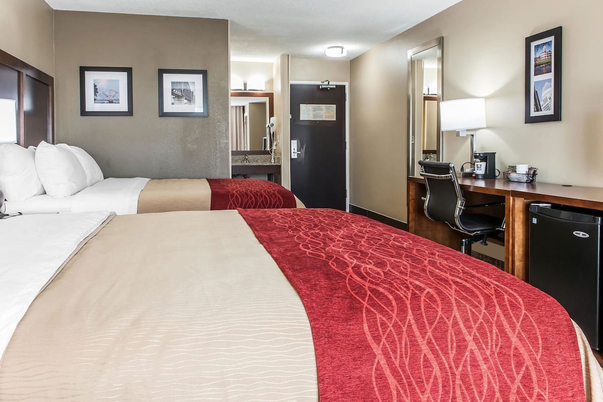 A hotel room with two beds, a desk, a chair, a refrigerator, and a mirror.