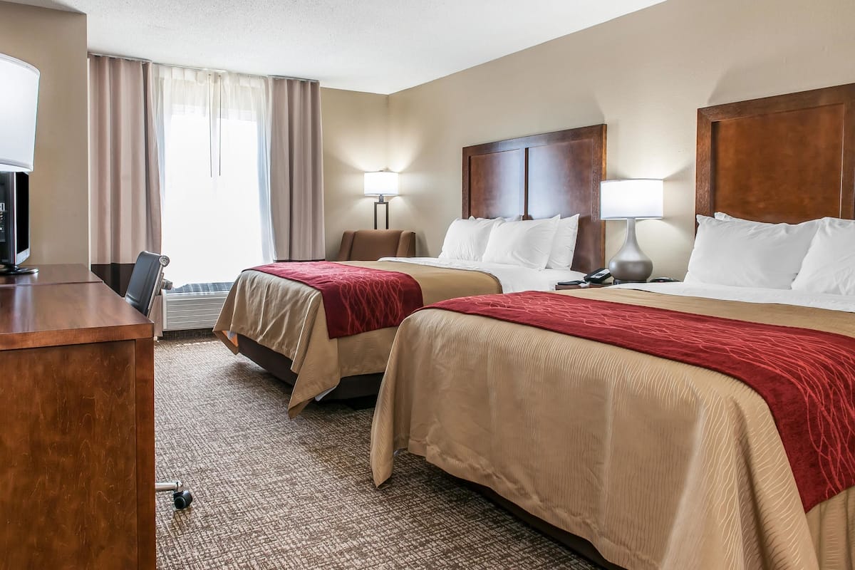 A hotel room with two beds, a desk, a TV, and a lamp.