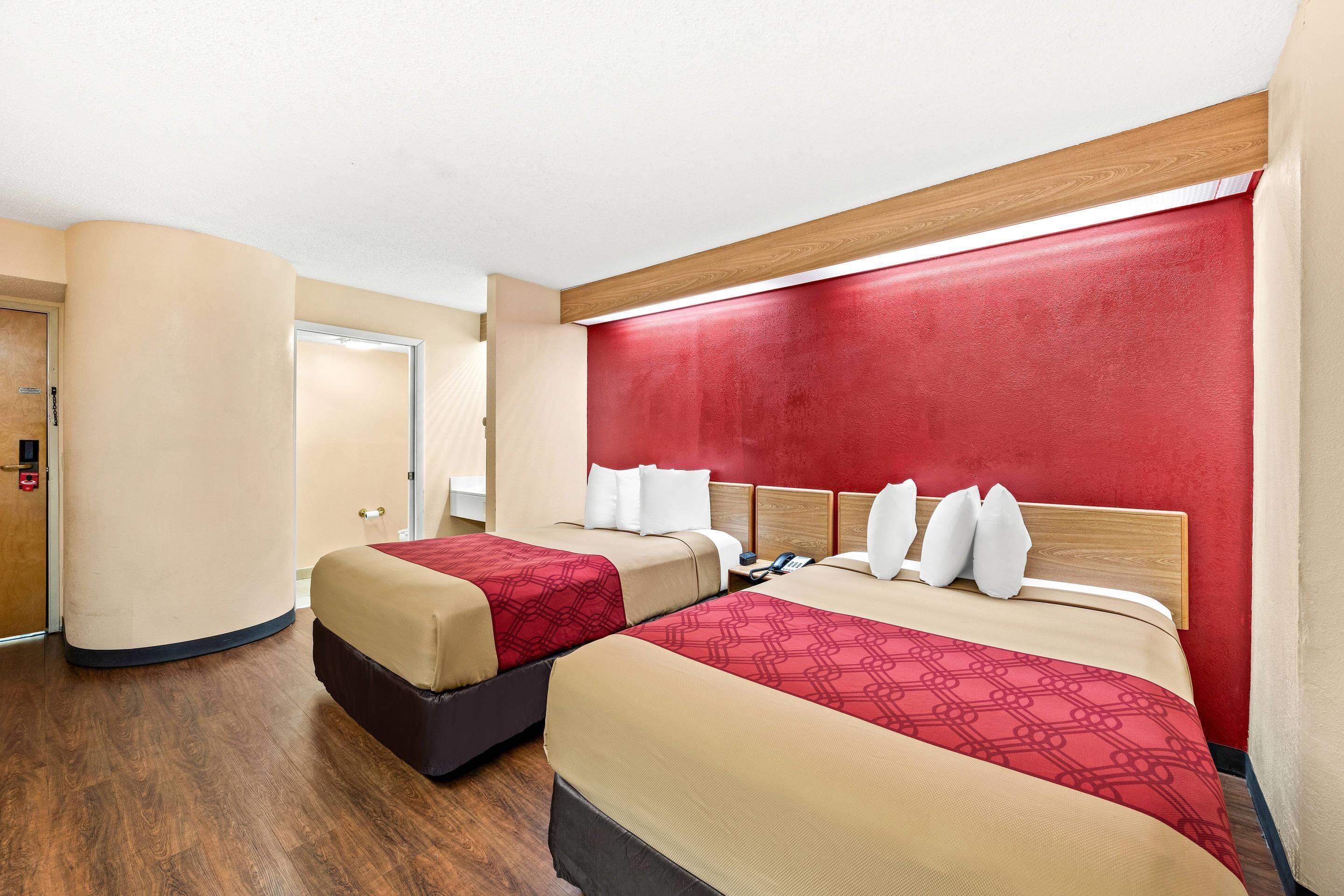 A hotel room with two beds, a wooden headboard, a red accent wall, and a wooden floor.