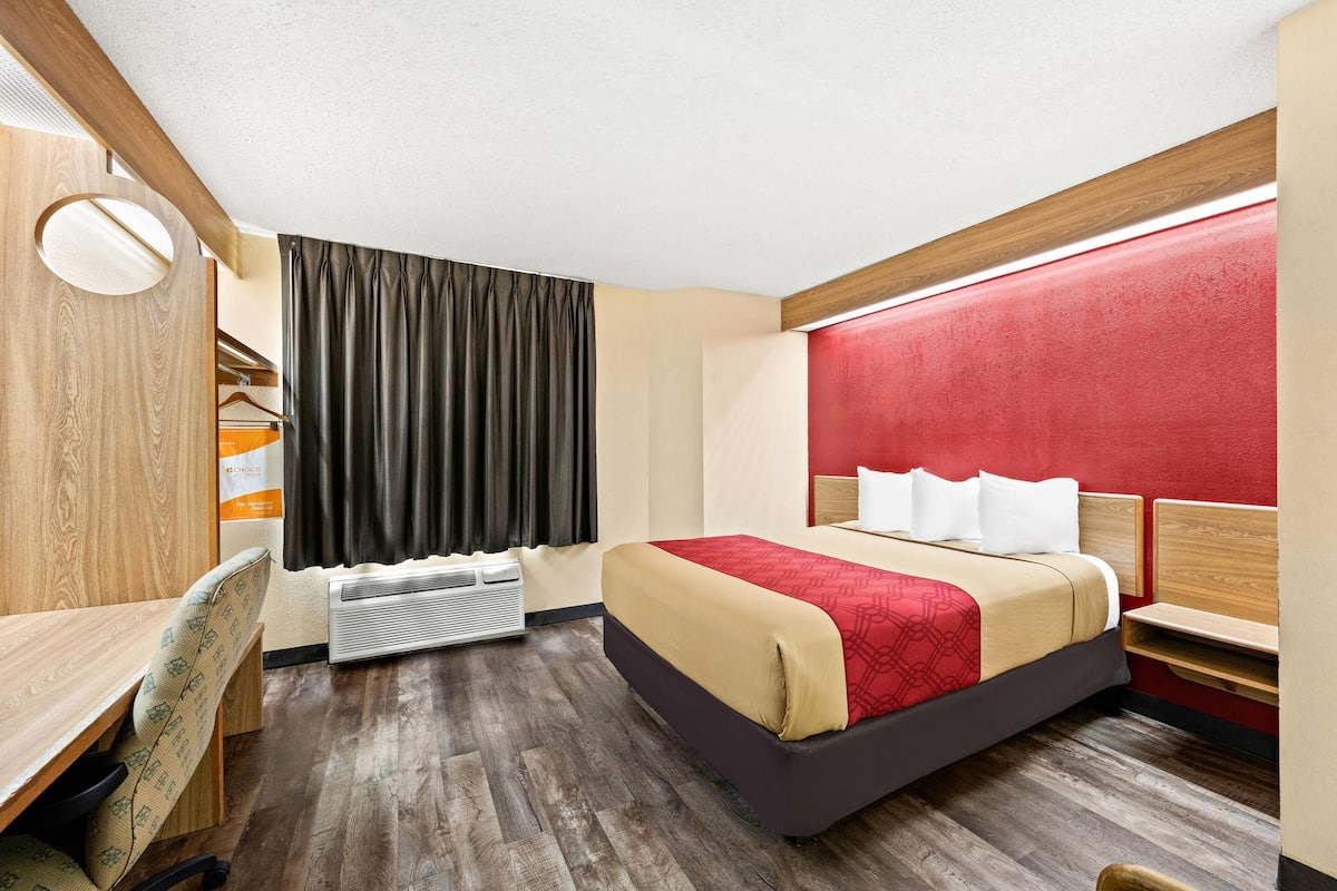 Une chambre d’hôtel avec un lit, un bureau, une chaise et une fenêtre avec des rideaux.