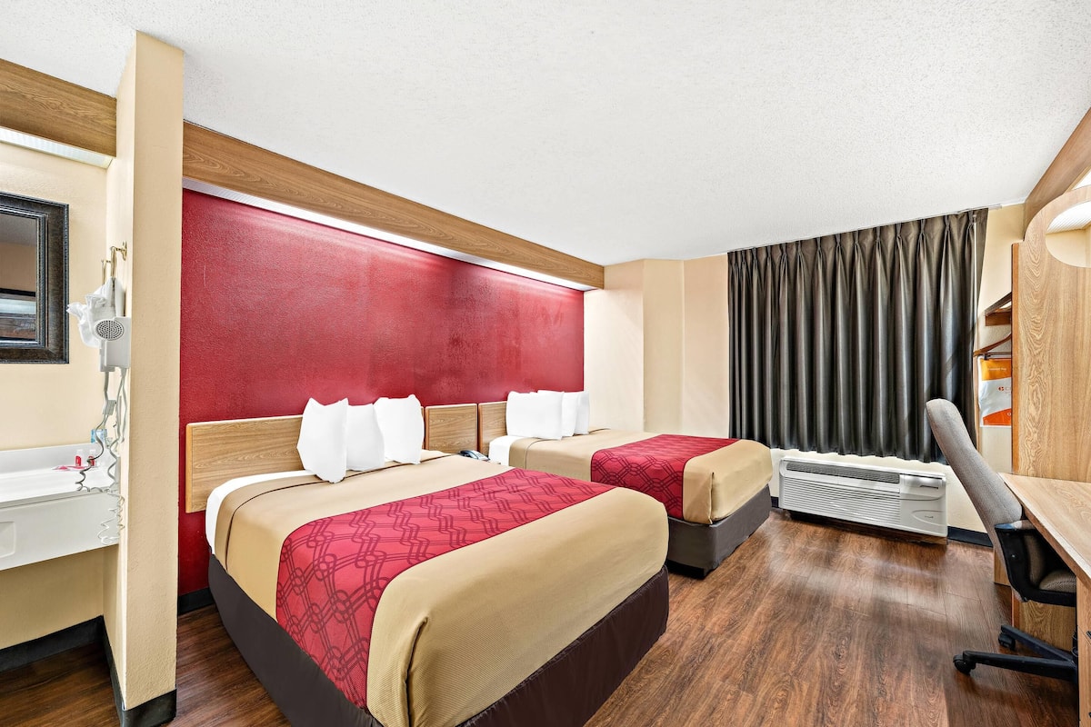 Une chambre d’hôtel avec deux lits, un bureau, une chaise, un miroir et une fenêtre avec des rideaux.