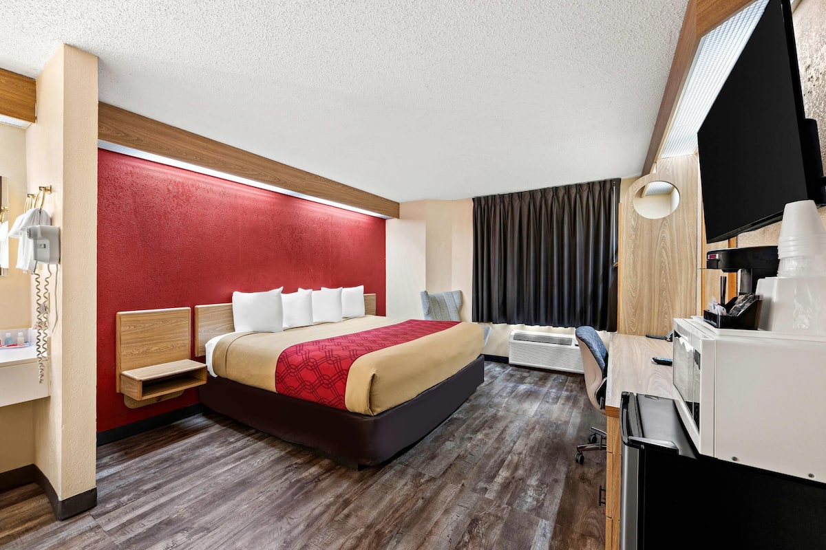 Une chambre d’hôtel comprenant un lit, une table de chevet, une lampe, une télévision et un bureau avec une chaise.