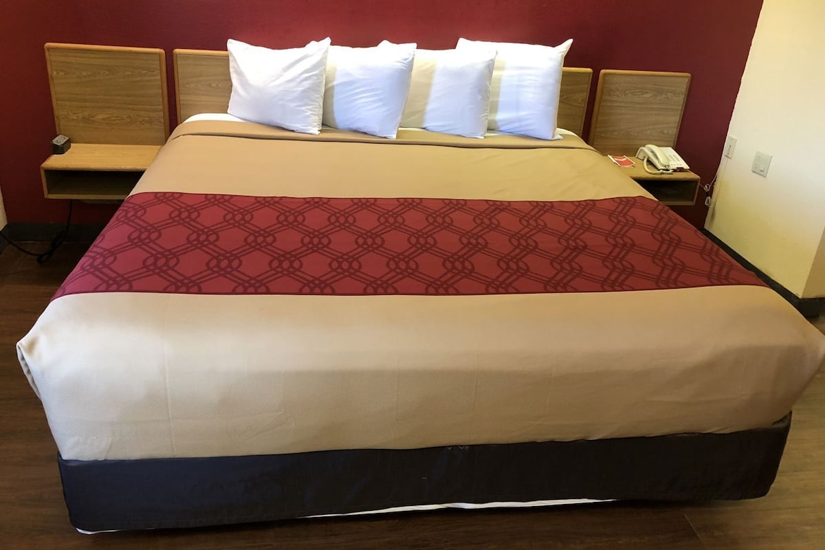 Une chambre d’hôtel avec un grand lit, une tête de lit en bois, une table de chevet avec un téléphone et un mur rouge.