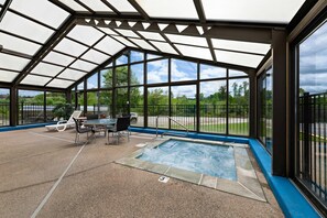 A covered outdoor swimming pool with a table and chairs, surrounded by glass walls and a metal railing. - Econo Lodge London North (London)