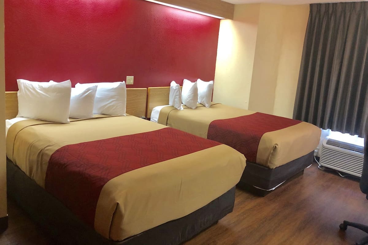 Une chambre d’hôtel avec deux lits, chacun recouvert d’une courtepointe rouge et beige, agrémentée d’oreillers blancs et dotée d’une tête de lit en bois.
