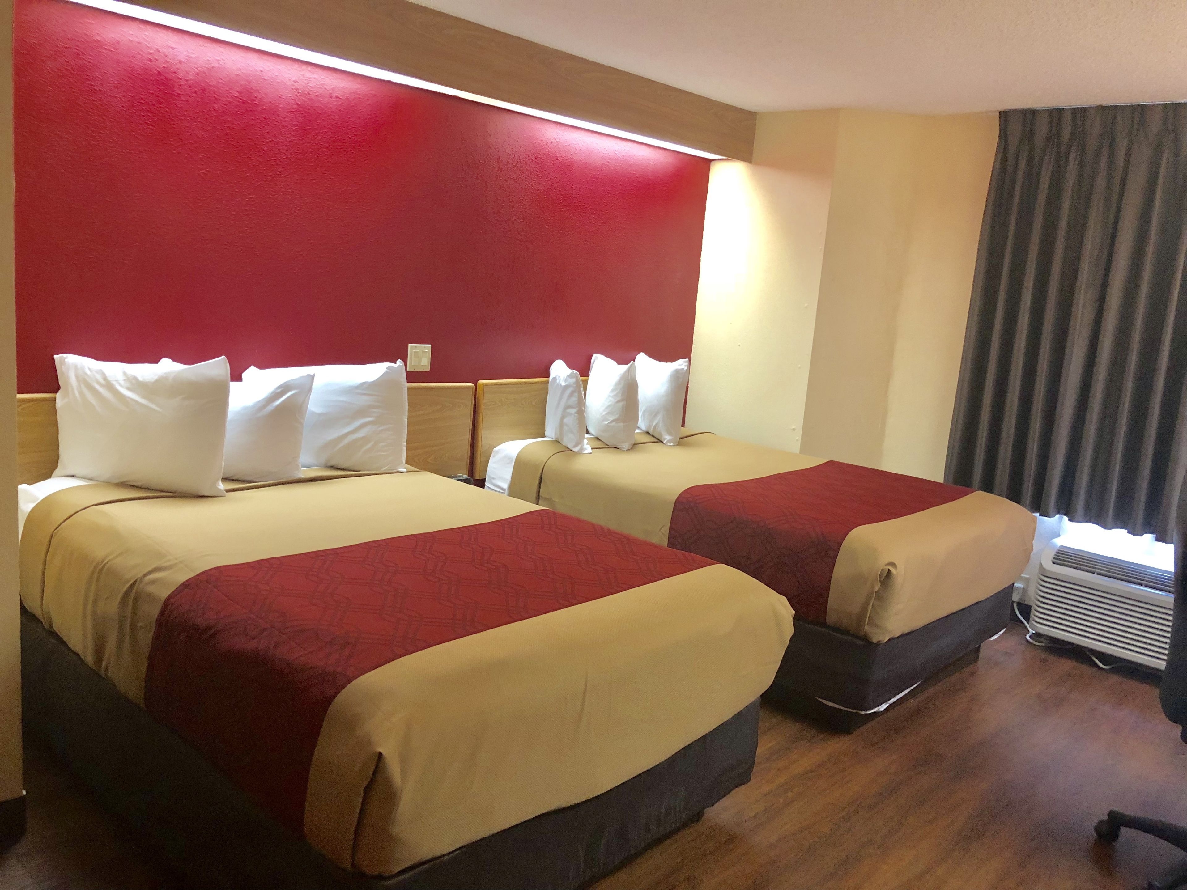A hotel room with two beds, each with white pillows and red and beige bedding.