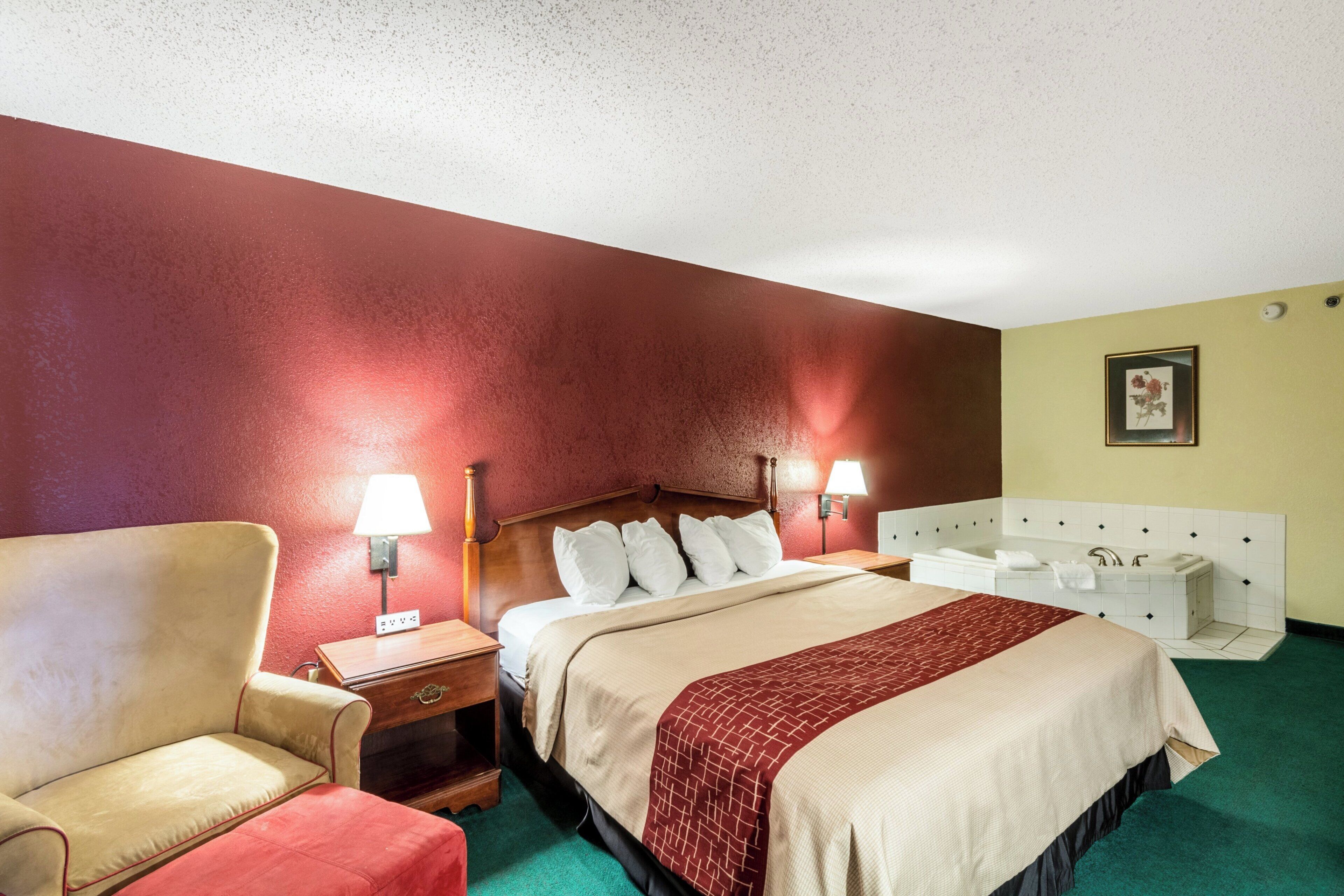 A hotel room with a bed, bedside tables, a chair, a desk, and a bathroom with a bathtub and sink.