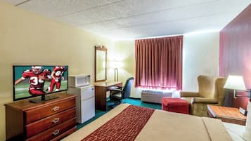 A hotel room with a bed, a desk, a chair, a television, a dresser, and a window with curtains.