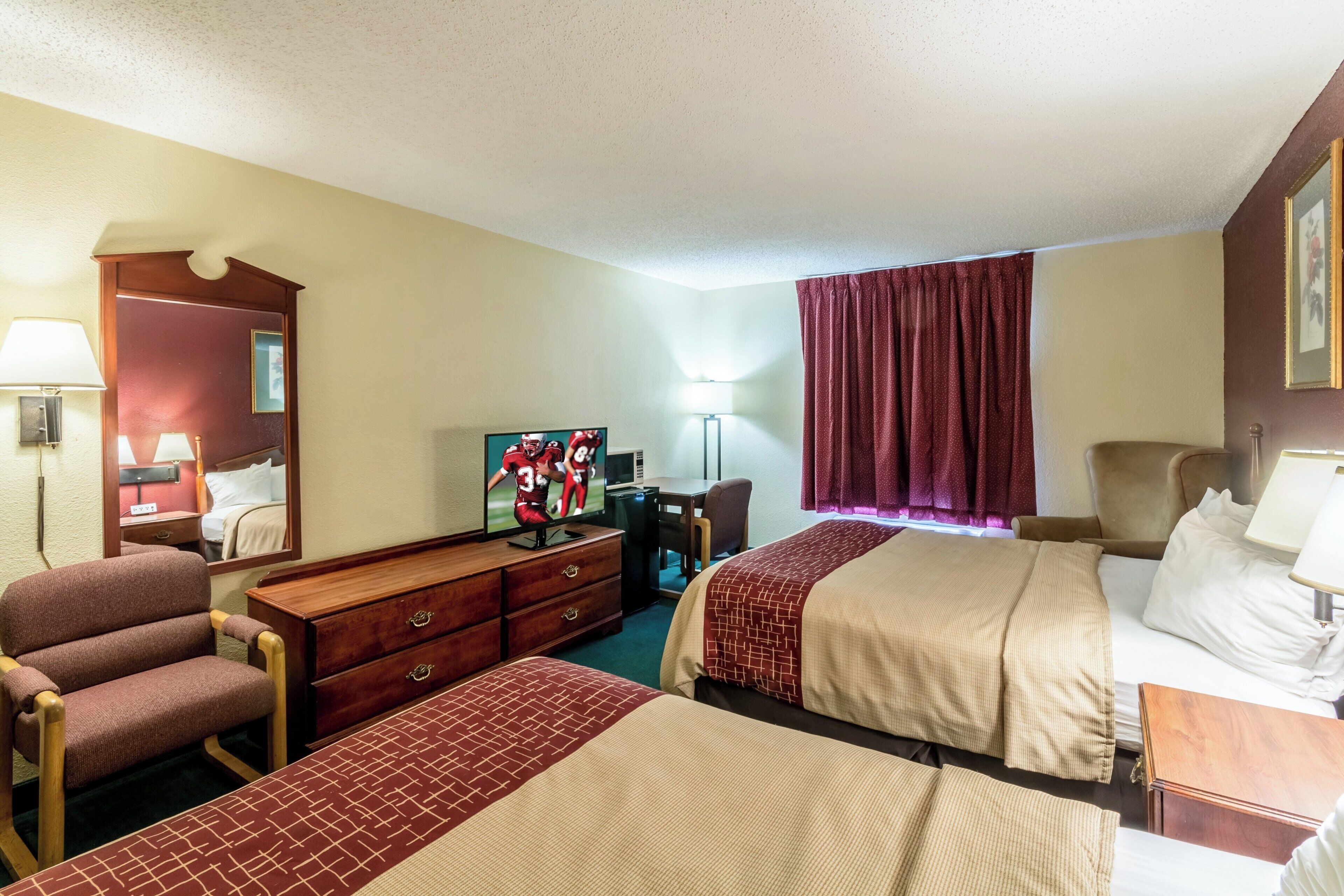 A hotel room with two beds, a desk, a chair, a television, and a mirror.