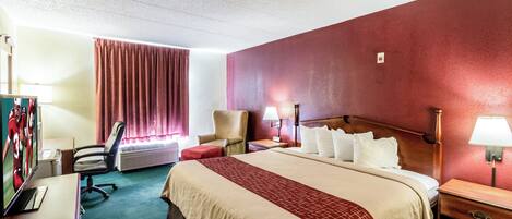 Una habitación de hotel con una cama, una silla, un escritorio con lámpara y un televisor.