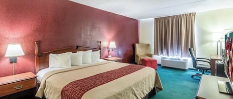 Habitación de hotel con una cama grande, dos lámparas de noche, una silla, un equipo de aire acondicionado y un escritorio con lámpara.