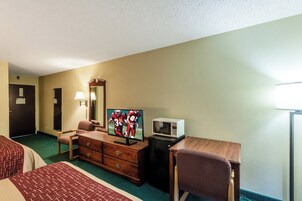 Habitación de hotel con una cama, un escritorio con televisor, microondas, cómoda, silla y lámpara.