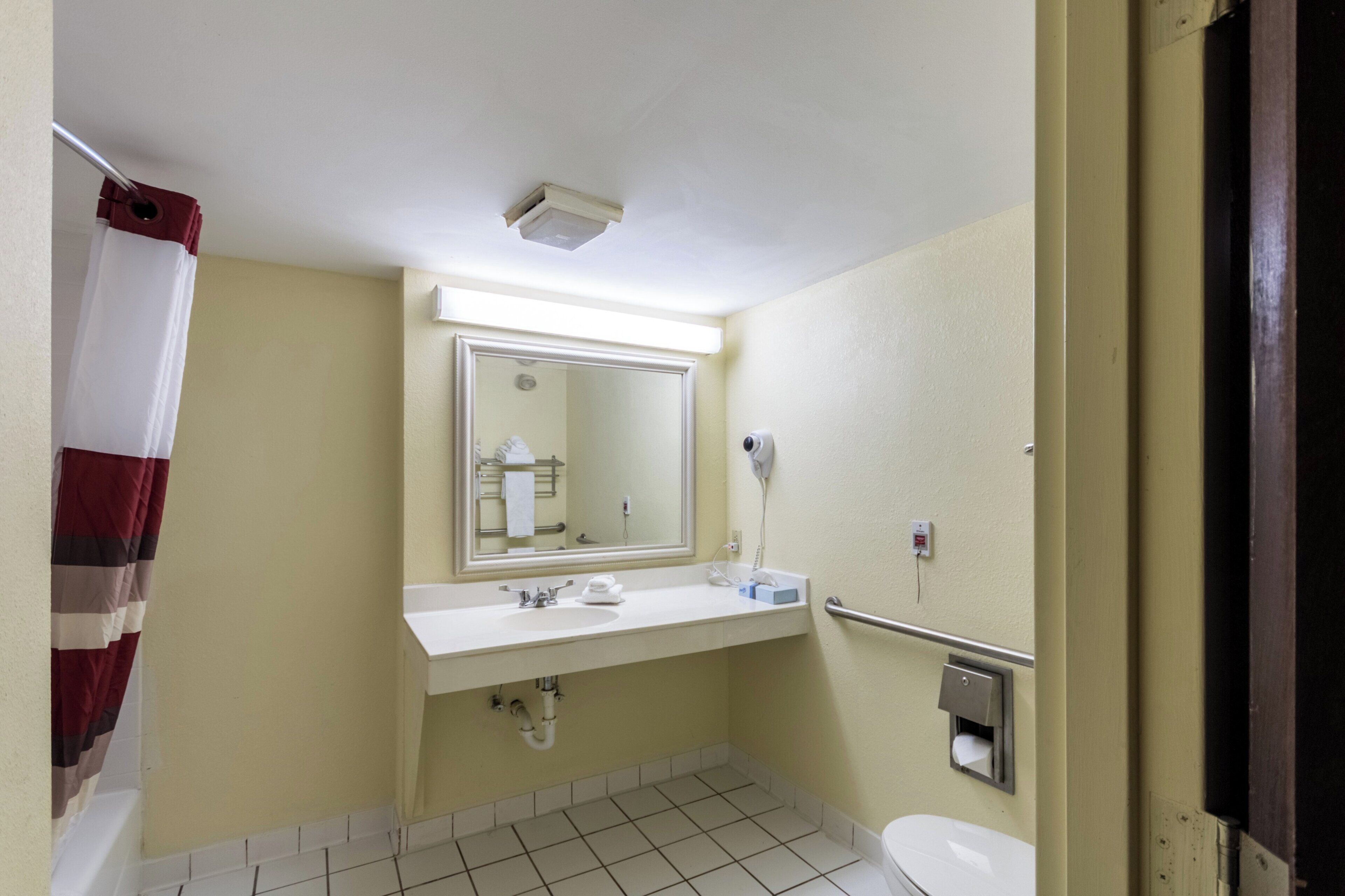 Un baño de hotel estándar con lavamanos, espejo, inodoro y toallero.