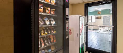 A vending machine with snacks and a refrigerator in a hallway.
