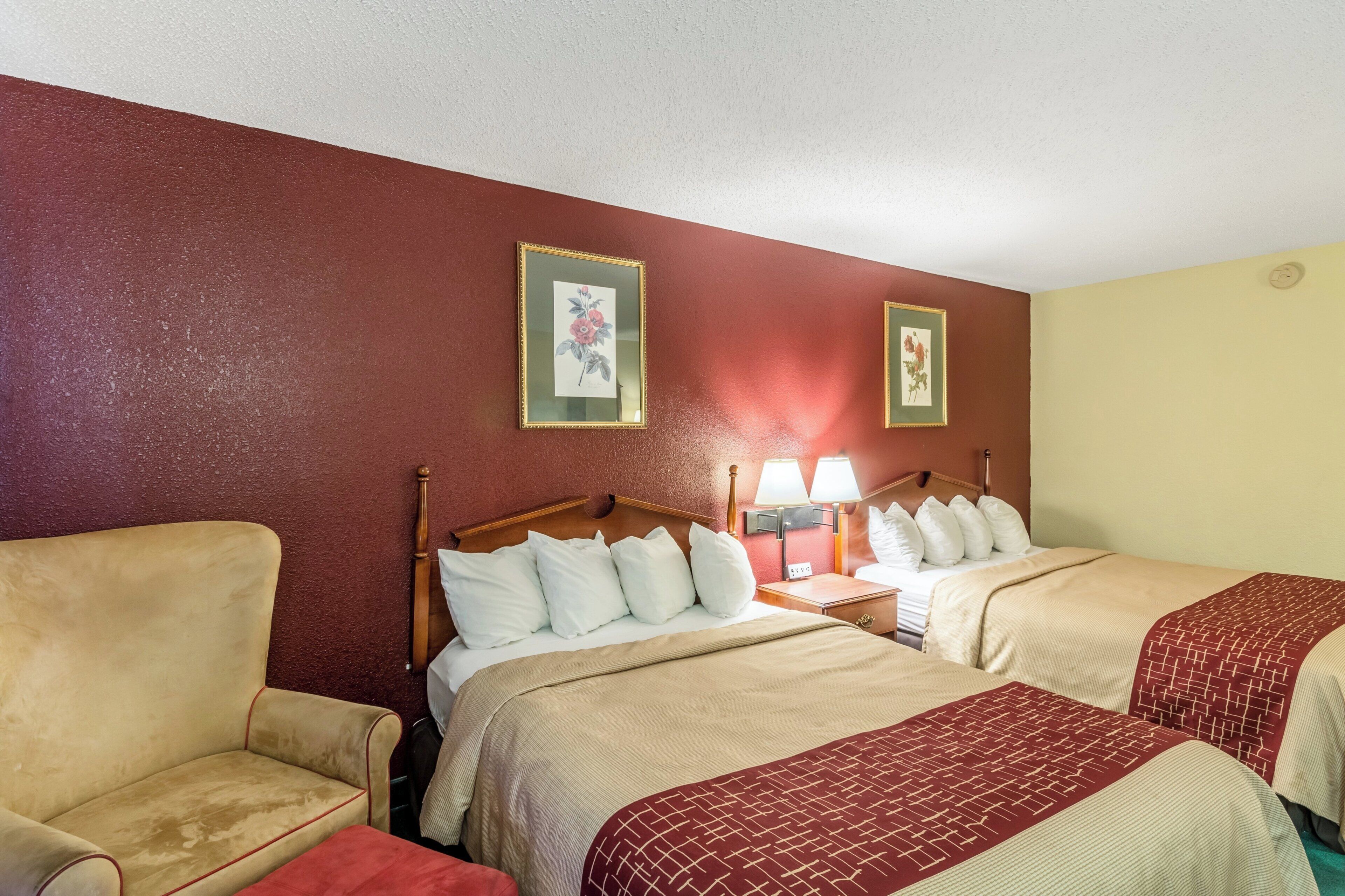 A hotel room with two beds, a chair, and a nightstand with lamps.