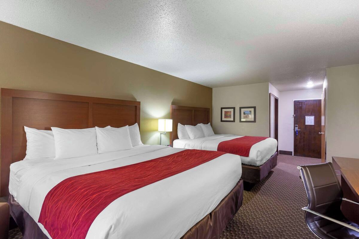 A hotel room with two beds, a desk, a chair, and a door.