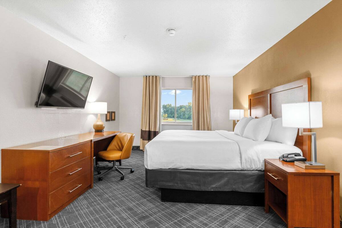 A hotel room with a bed, desk, chair, TV, and window with curtains.