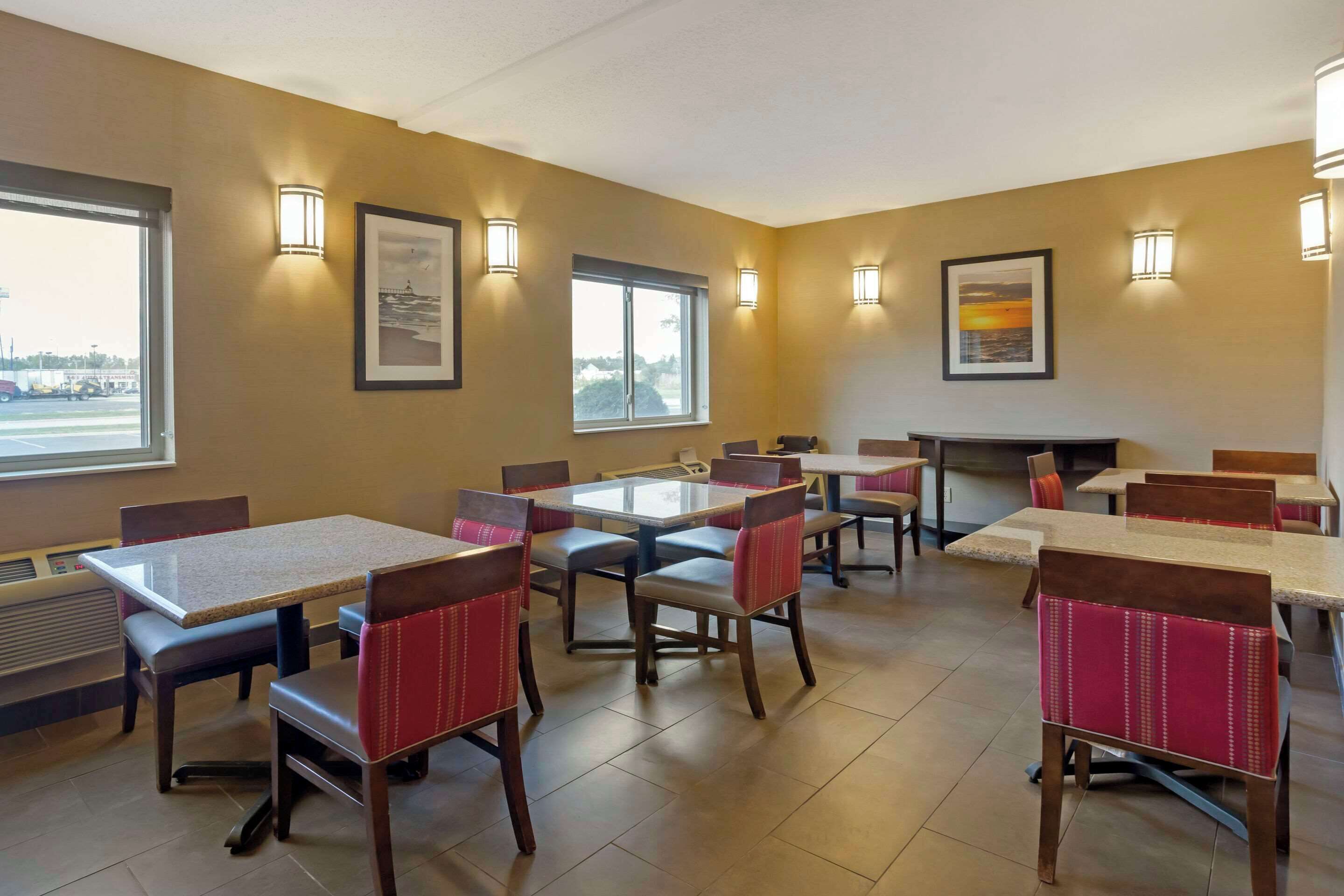 A dining area with multiple tables and chairs, framed pictures on the walls, and large windows.