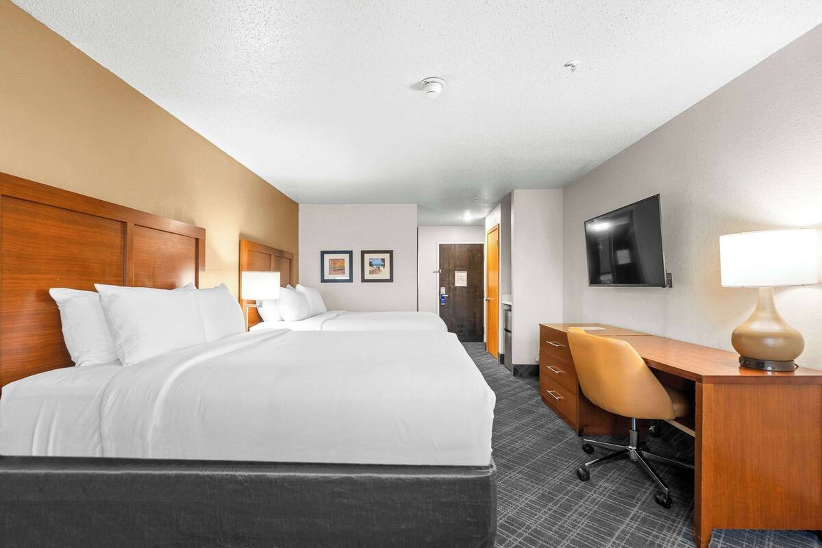 A hotel room with two beds, a desk, a chair, a TV, and a lamp.